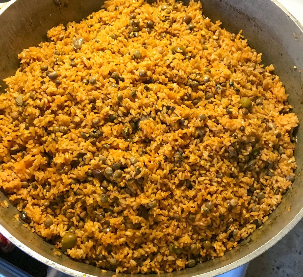 A caldero full of golden-orange arroz con gandules with pigeon peas and green olives