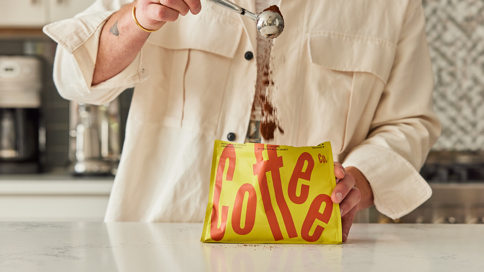 Person pouring coffee from a yellow bag labeled 'Coffee' into a cup in a kitchen.