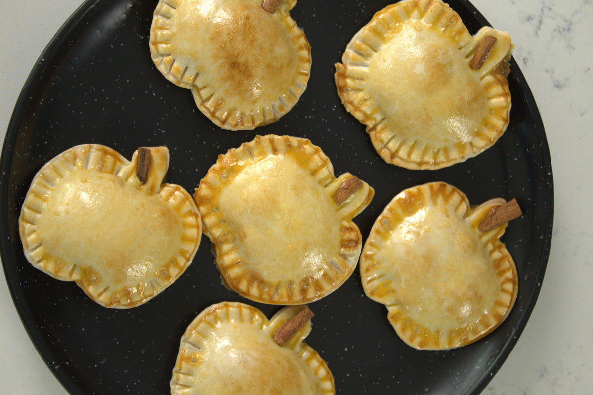 Baked guava empanadas shaped like little pumpkins, with cinnamon-stick stems, on a round black platter